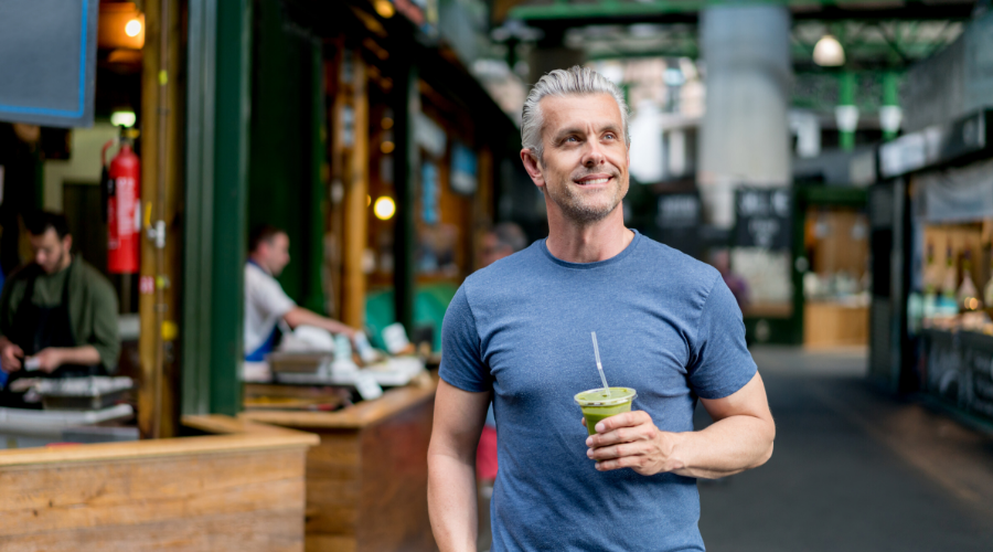 Sportieve man met grijs haar drinkt smoothie in markthal - Bodystore.nl