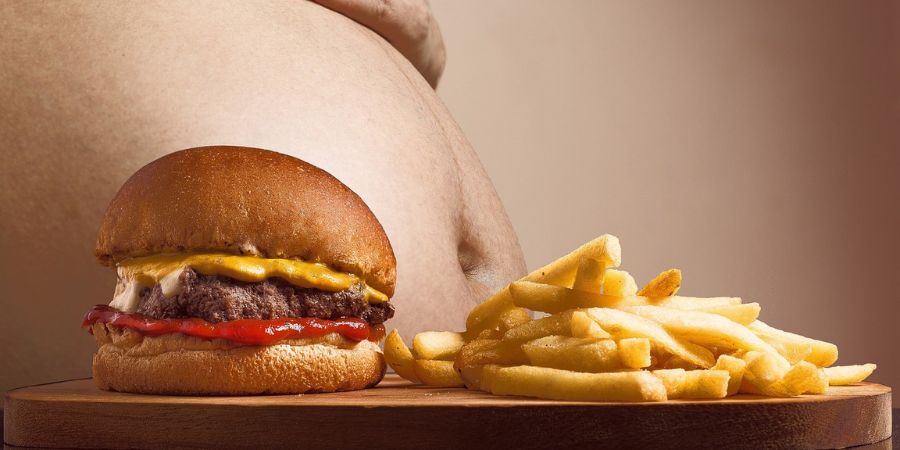 Man met dikke buik, bij een tafel met frietjes en hamburger